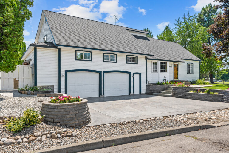 Charming white house with a double garage, landscaped yard, and a modern driveway.