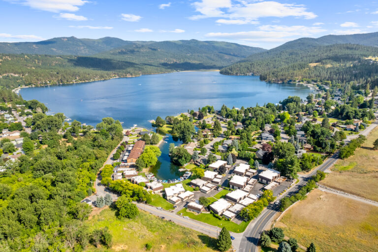 Aerial view of a scenic lakeside community surrounded by lush greenery and mountains under a bright blue sky.