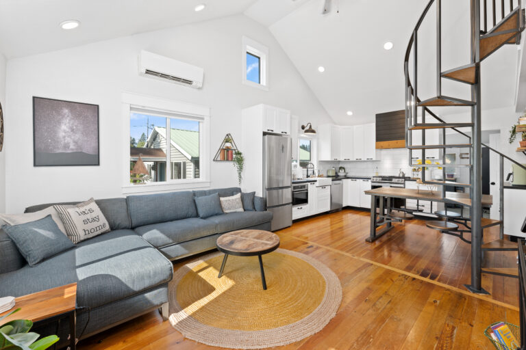 Modern open-concept living space with a cozy sectional, rustic wood flooring, and a stylish spiral staircase leading to a loft.