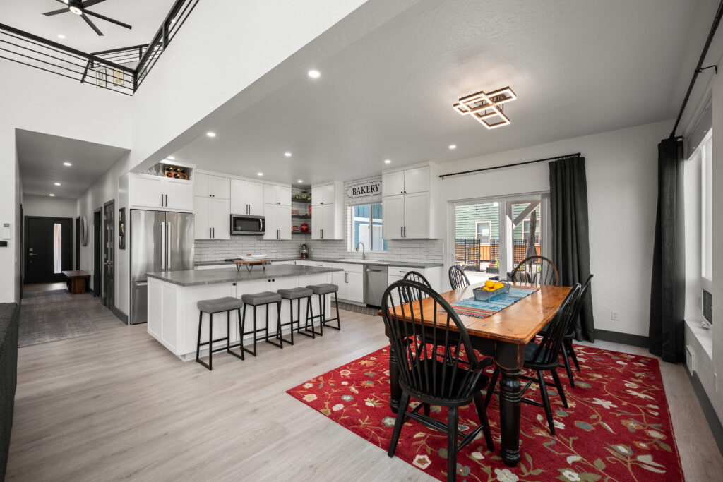Bright open-concept kitchen and dining area with modern lighting, white cabinets, and a cozy red rug.